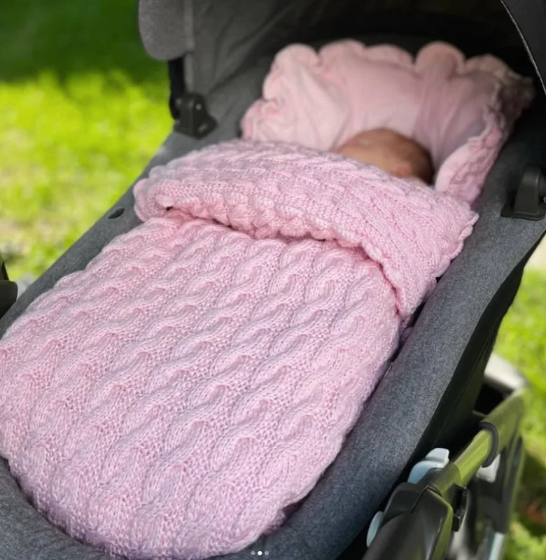 Sovende baby i rosa strikket vognpose i vognen ute i hagen